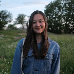 Ung kvinne i denimjakke som står på et grønt jorde utendørs Ung kvinne med langt mørkt hår iført en denimjakke som står i et grønn åker.