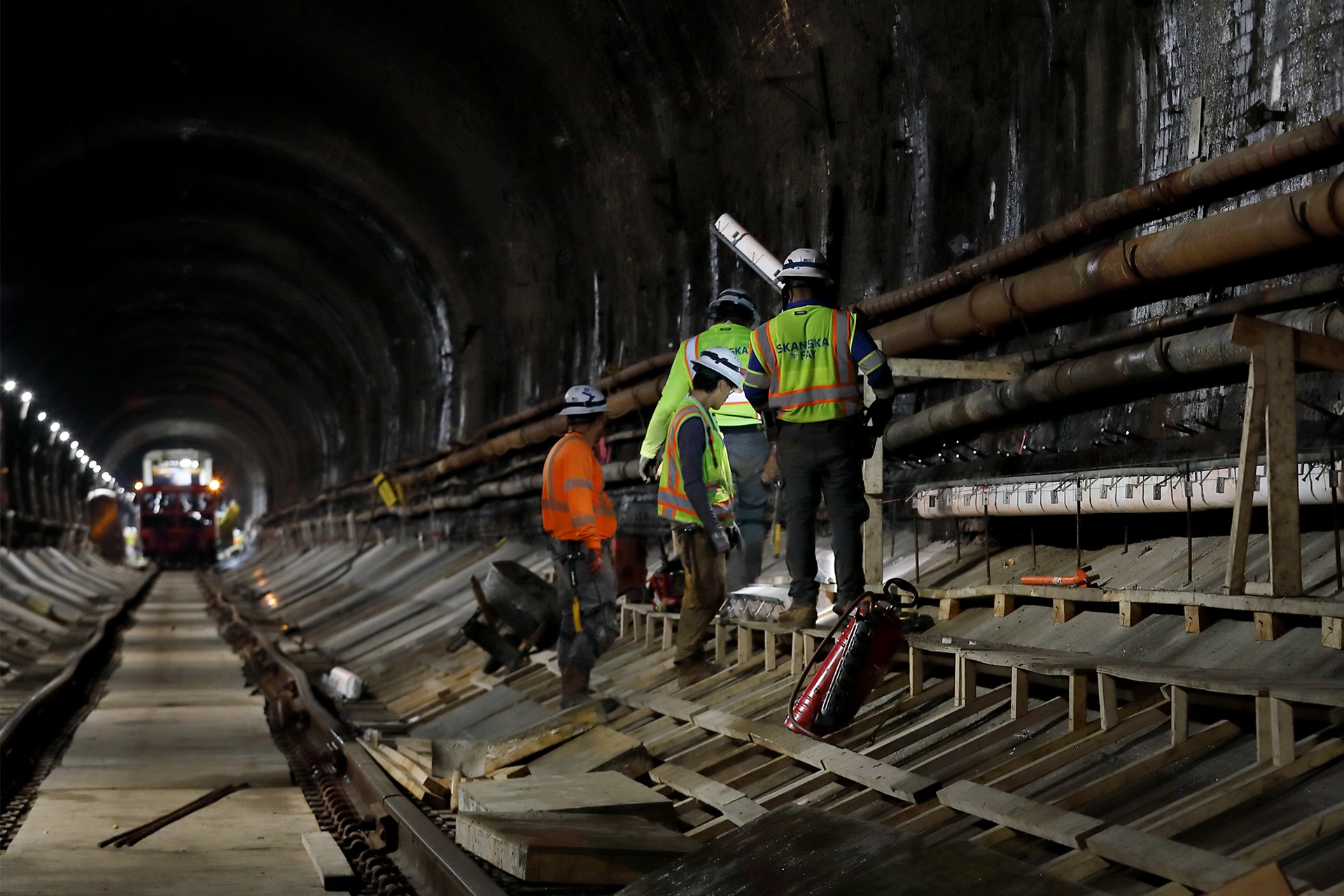 Tunnel construction workers inspecting railway tracks at night Workers wearing safety gear inspect construction inside a dark railway tunnel.