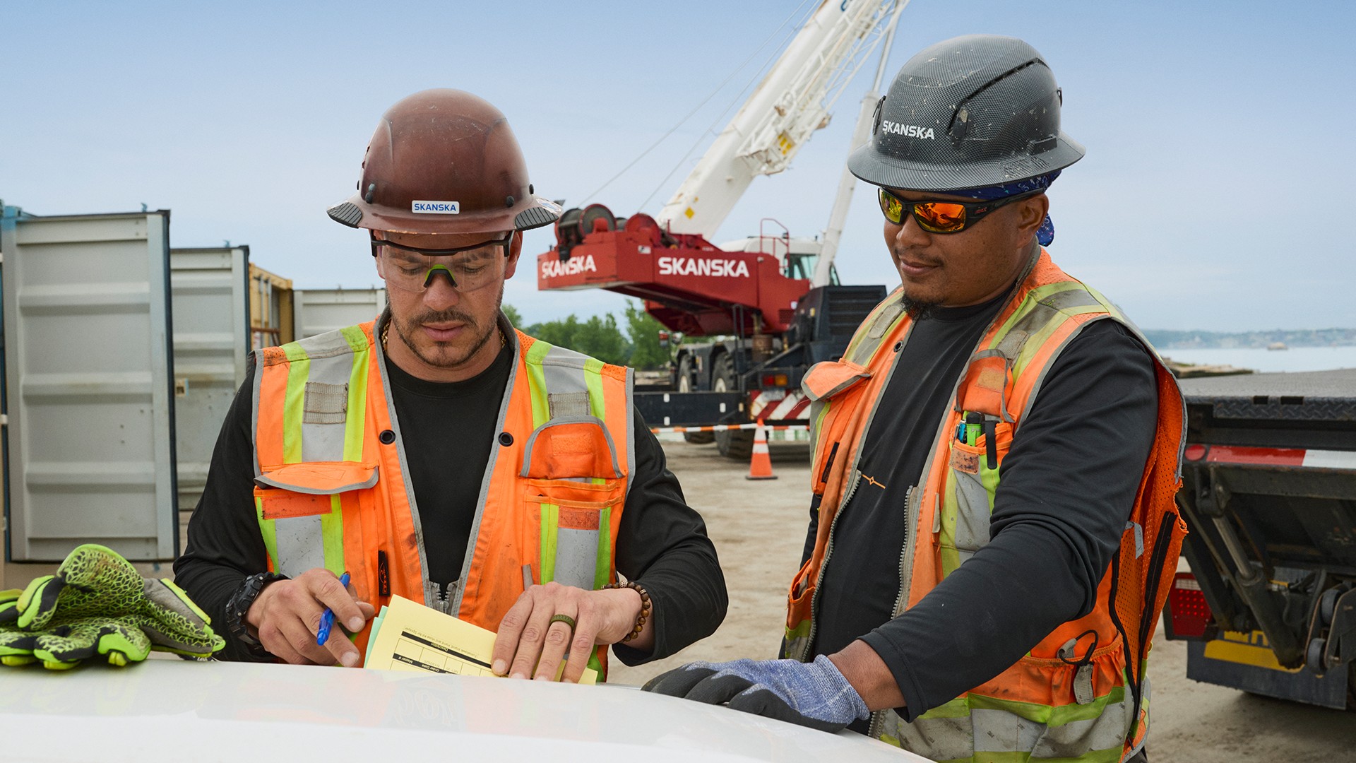 Construction workers wearing safety gear at a site meeting Two construction workers in safety vests and helmets reviewing documents at site.