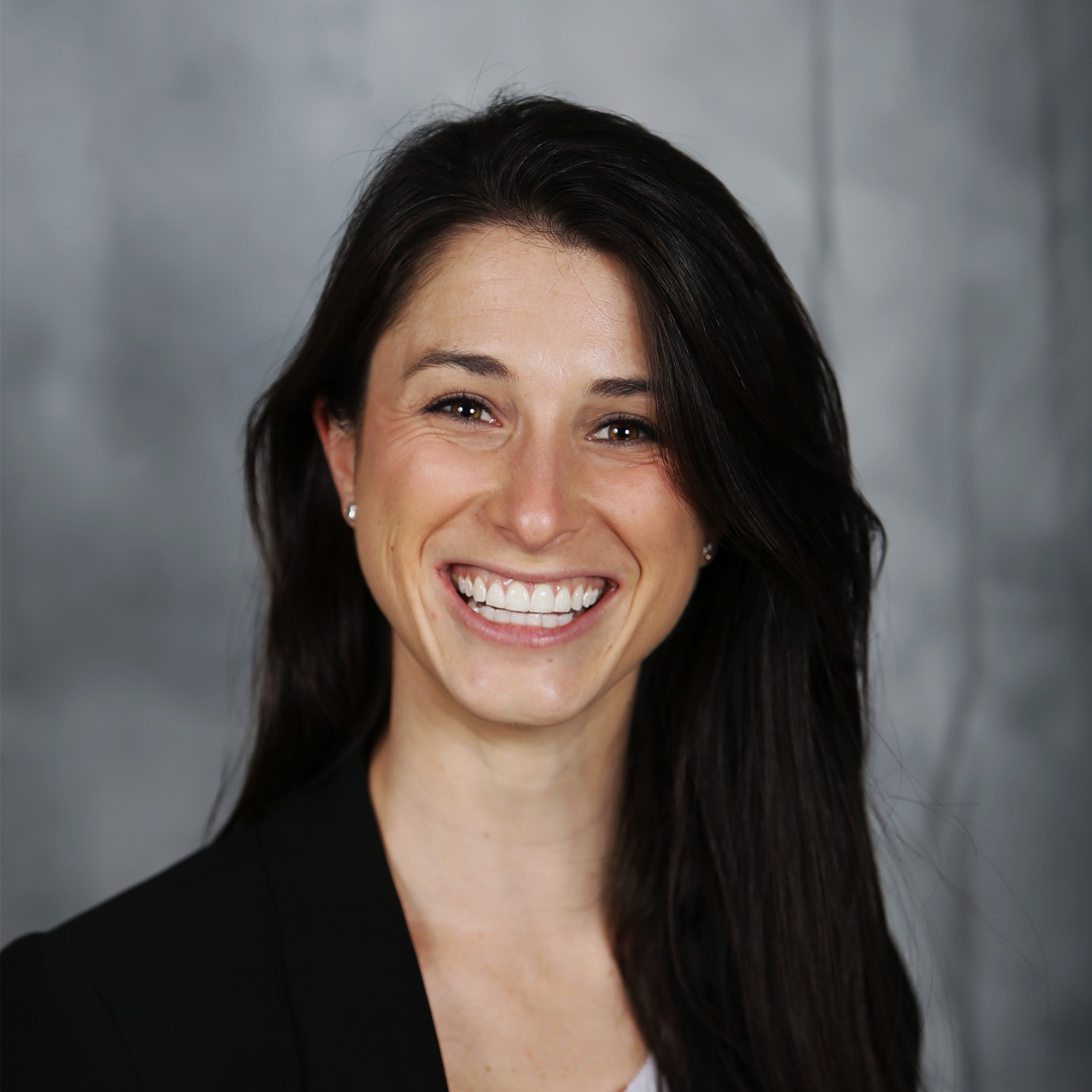 Professional woman with long dark hair in black blazer portrait Professional woman with long dark hair wearing a black blazer against gray background.