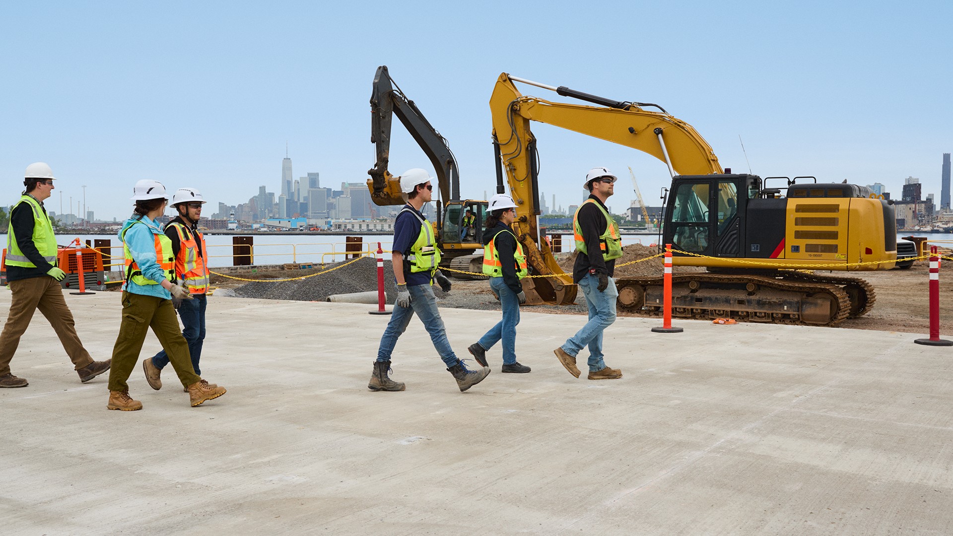 Construction workers walking at urban site with excavators Construction workers in safety gear walking at a waterfront site with excavators.