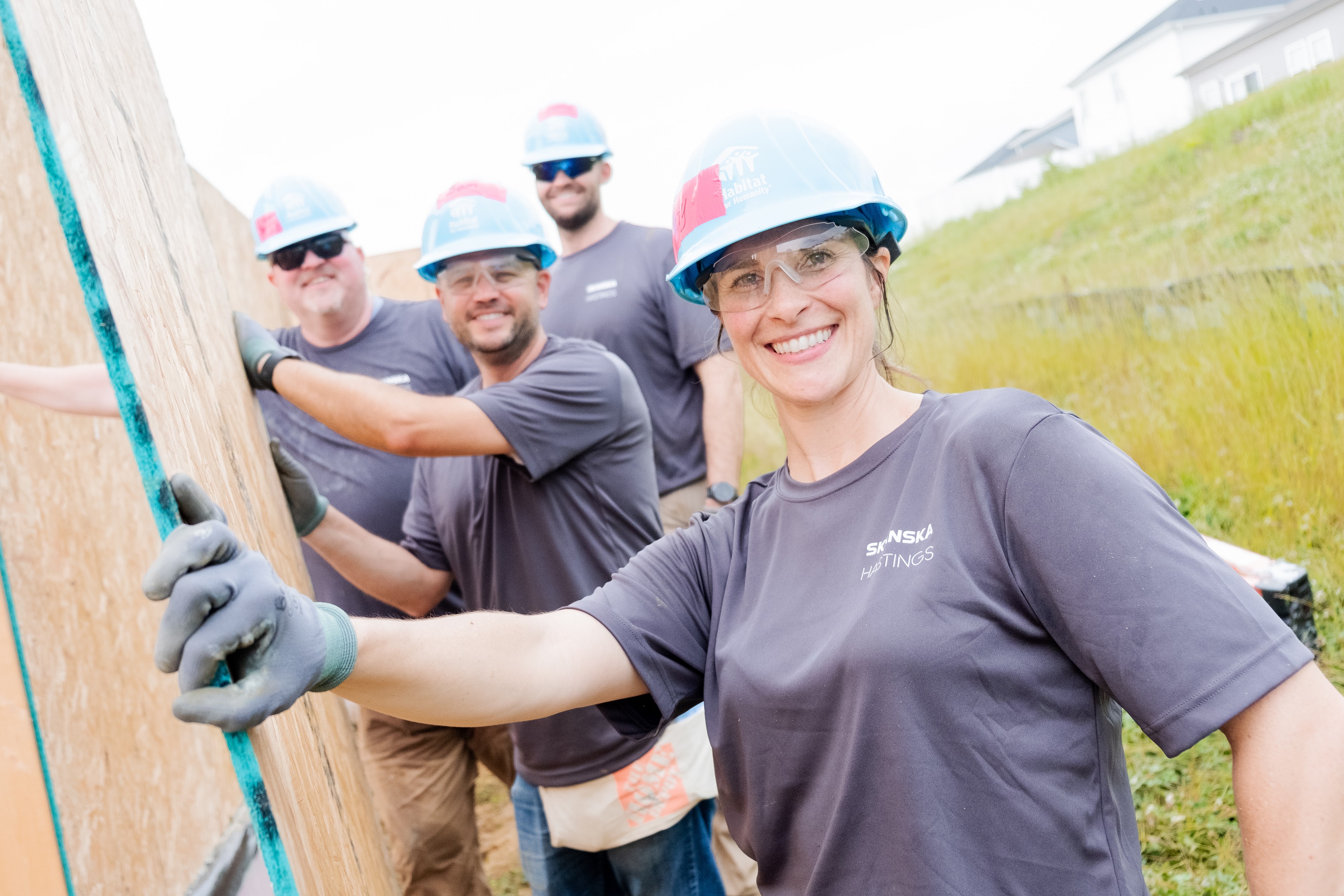Construction workers wearing helmets and gloves lifting wooden beams outdoors.