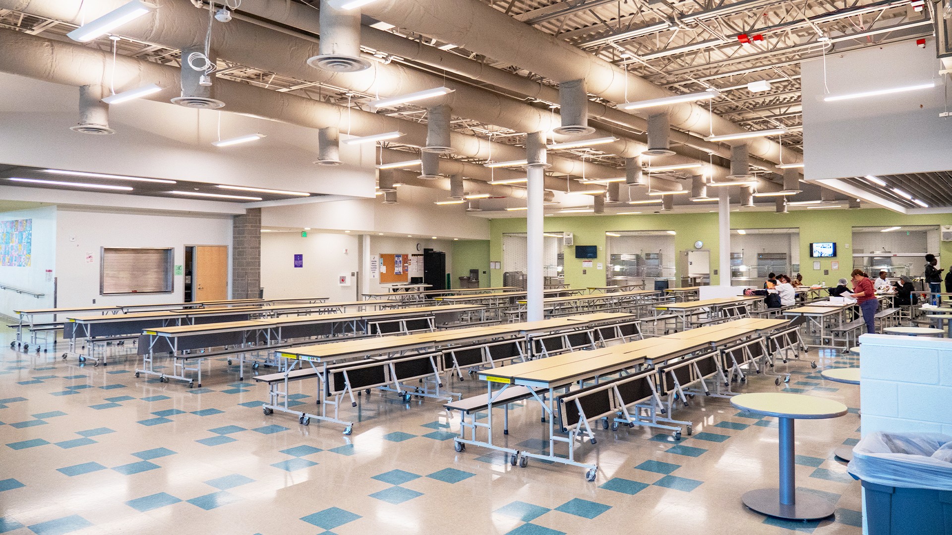 School Library Interior with Wooden Ceiling and Bookshelves School cafeteria with rows of chairs, tables, and students eating.