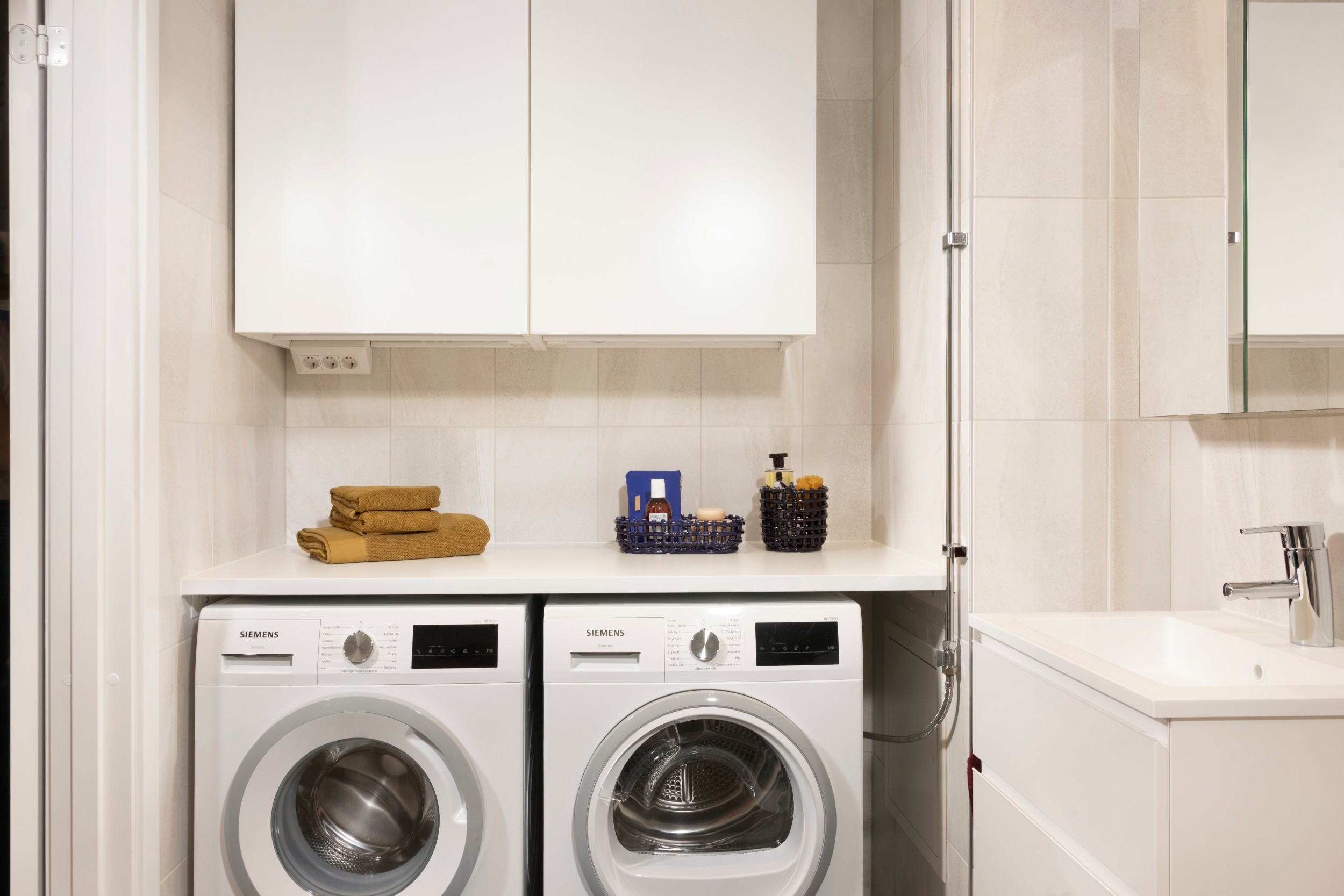 Modern laundry room with Siemens washer and dryer, white cabinets, and neatly folded towels.