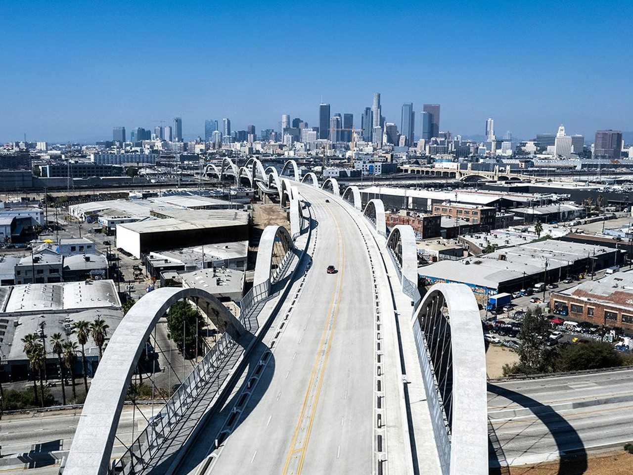 Downtown LA Skyline with Historic Sixth Street Bridge View Aerial view of Los Angeles skyline with a modern arched bridge and clear blue sky.