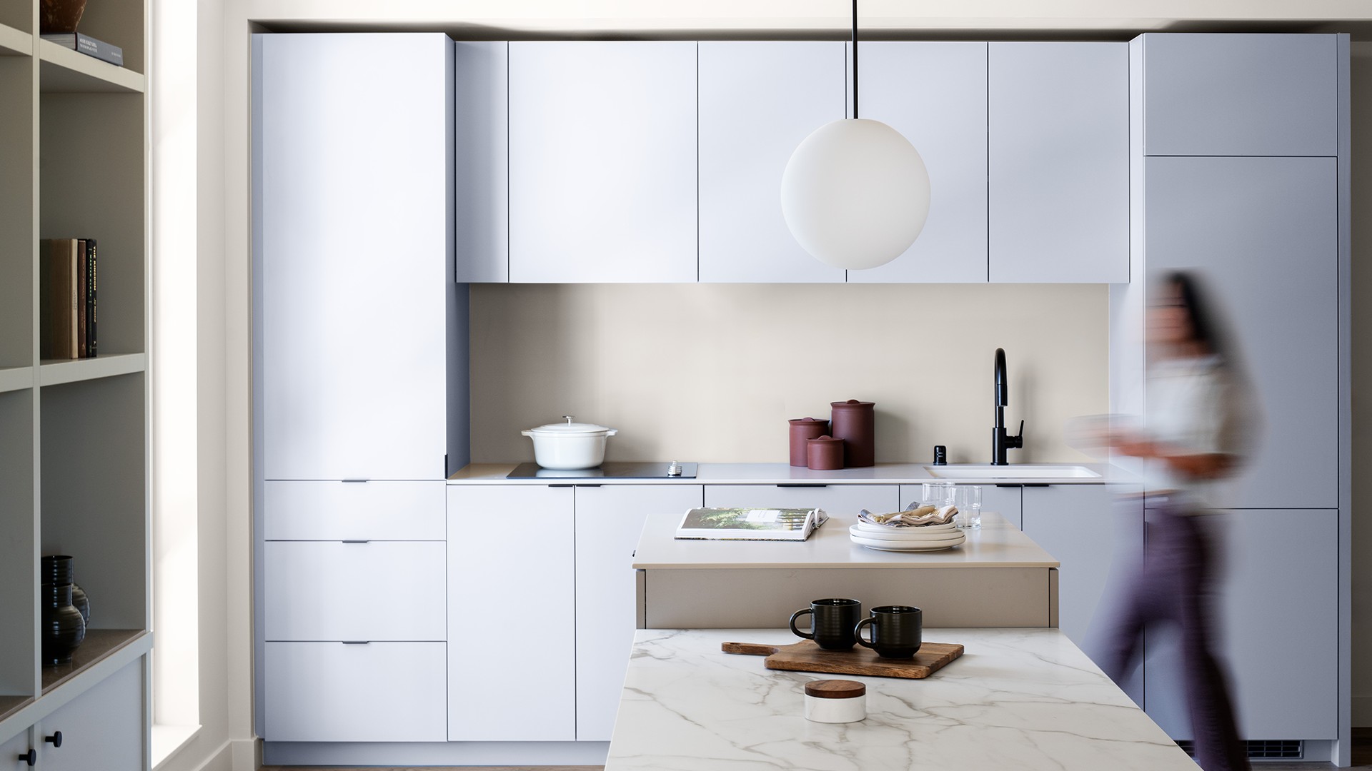 Modern Minimalist White Kitchen with Marble Island and Pendant Light Modern white kitchen with marble countertop, sleek cabinets, and a blurred person.