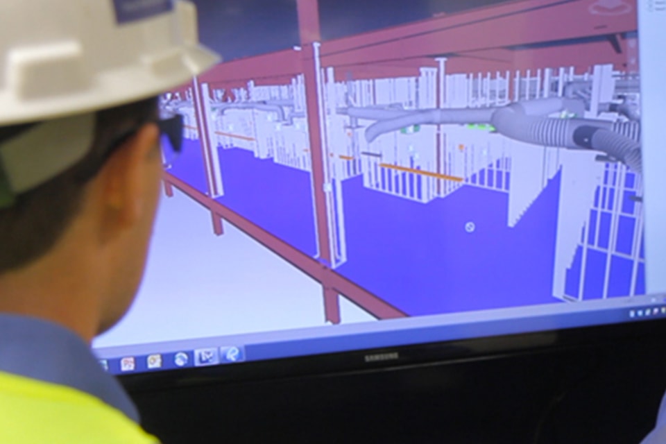Engineer in a hard hat reviewing 3D building model on a computer screen.