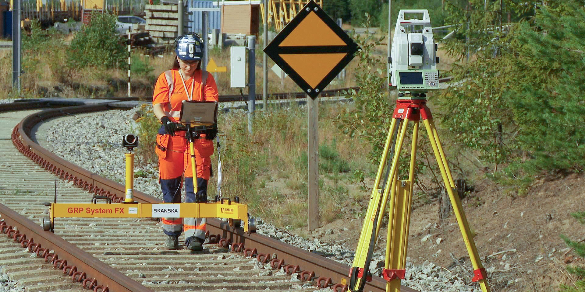 Railway Surveying: Precision Engineering in Action En landmåler i oransje sikkerhetsutstyr bruker utstyr på et jernbanespor ved siden av en stativmontert enhet.