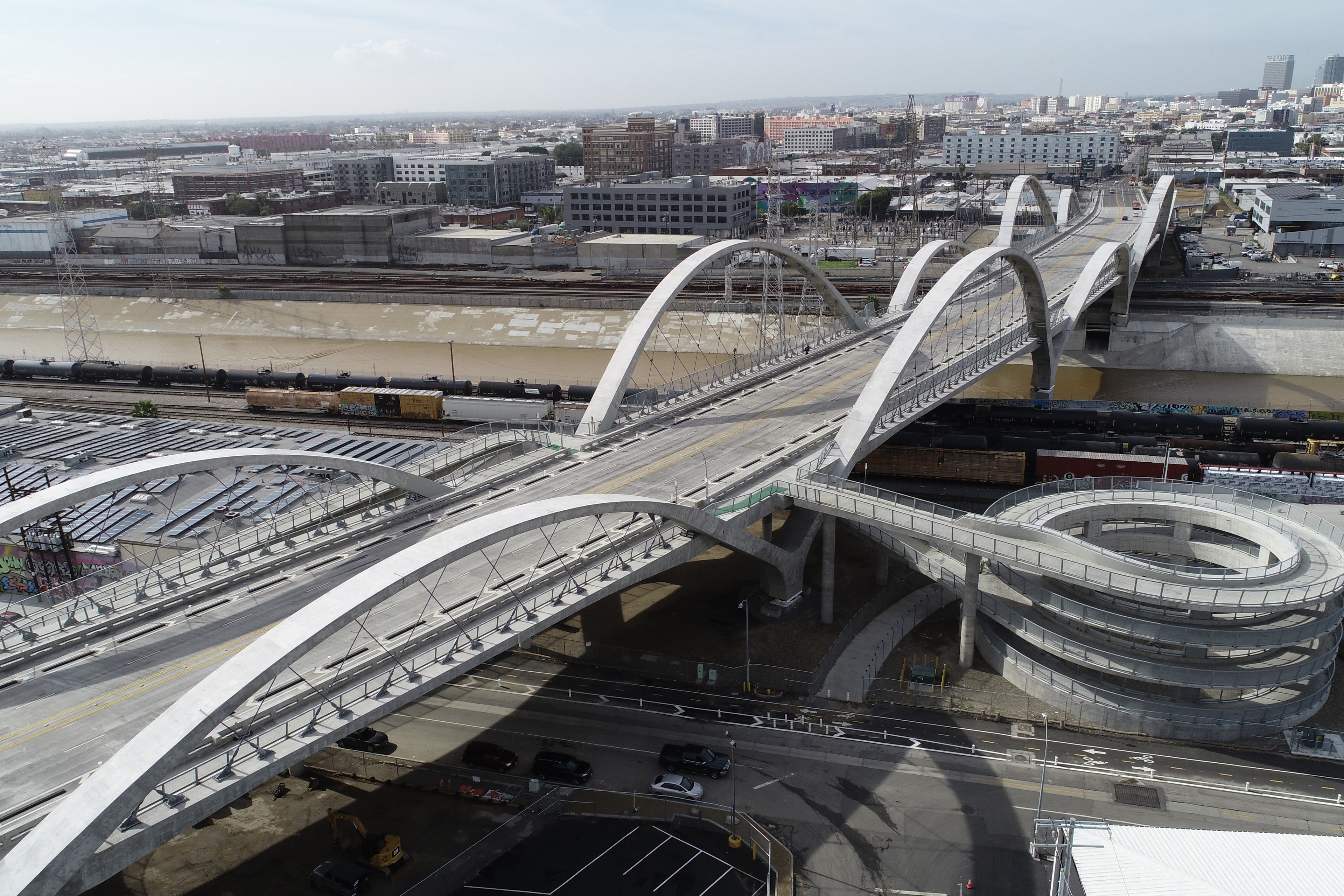 Aerial view of a modern arched bridge over a river in an urban industrial area.