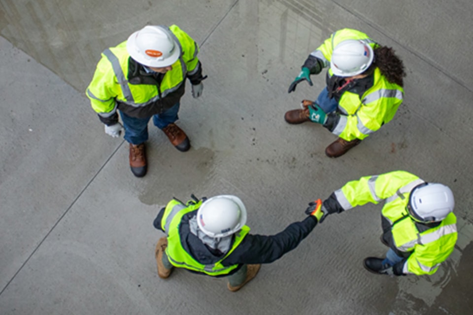 Top view of four construction workers in safety gear on a concrete surface at site.