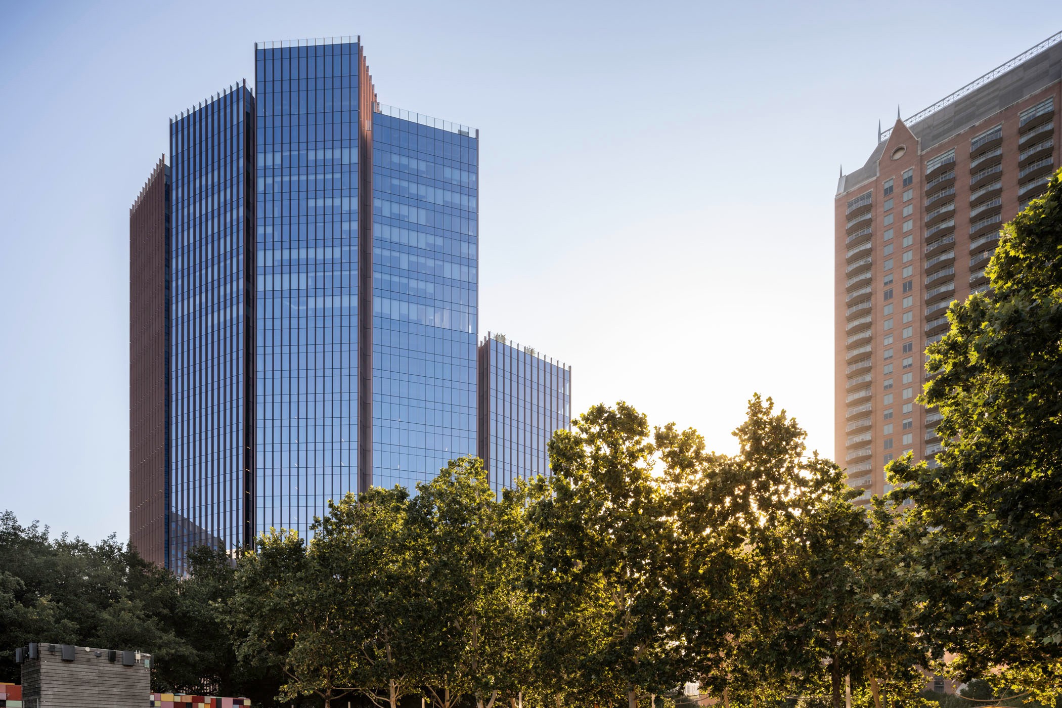 Modern Glass Office Buildings with Trees in Urban Skyline Modern glass skyscrapers with surrounding green trees under a clear blue sky.