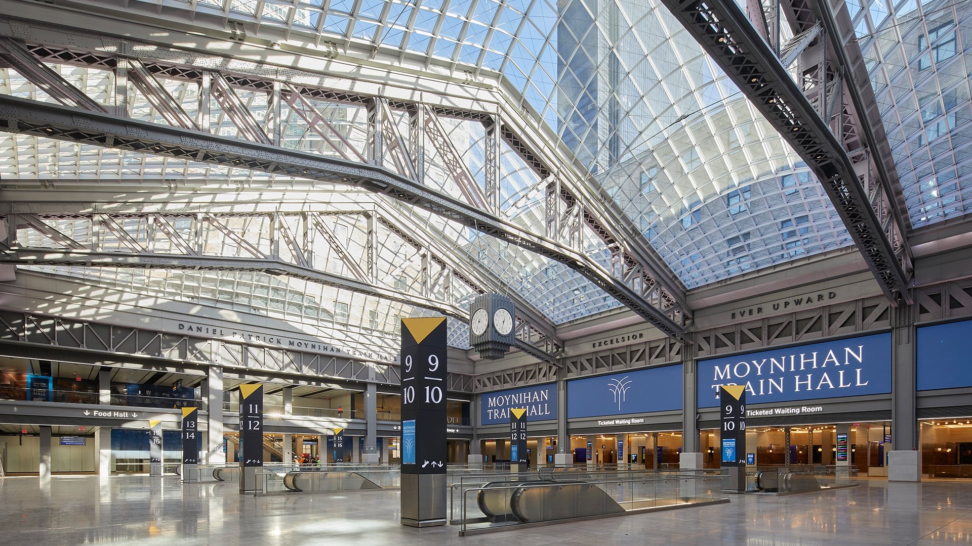 Interior view of Moynihan Train Hall with glass ceiling and digital signage.