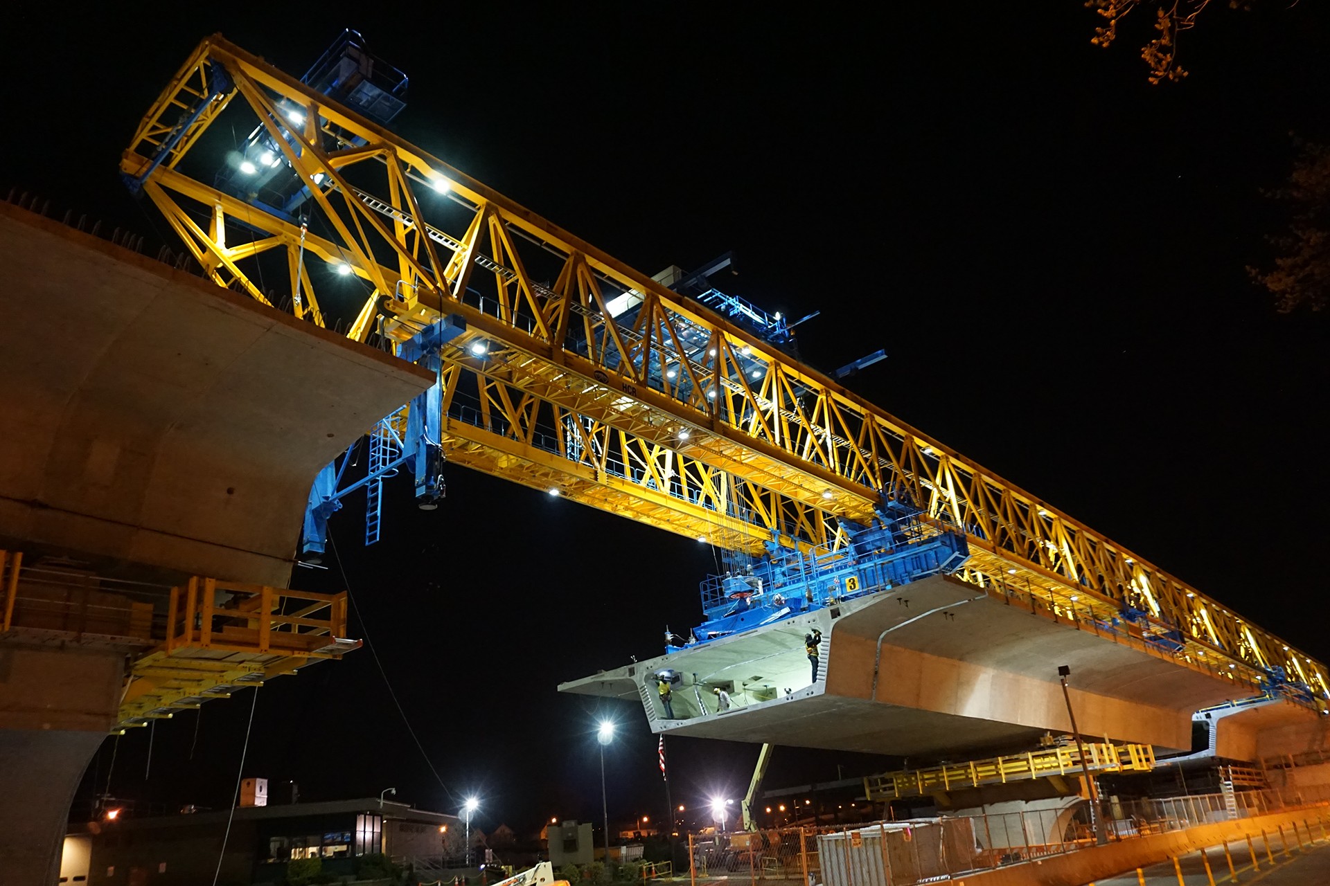 Tunnel construction workers inspecting roadway at night Yellow construction crane assembling a bridge at night with bright lighting.