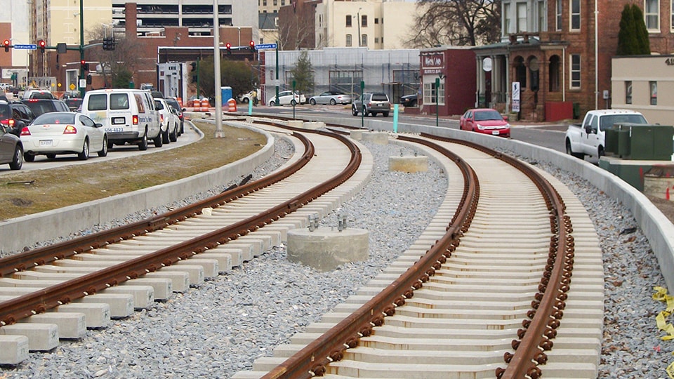 Urban railway tracks curving through city street with traffic Curved urban railway tracks with concrete sleepers alongside a busy city street.