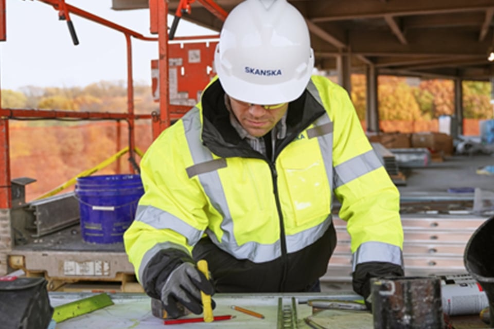 Construction worker in high-visibility jacket and helmet reviewing blueprints on site.