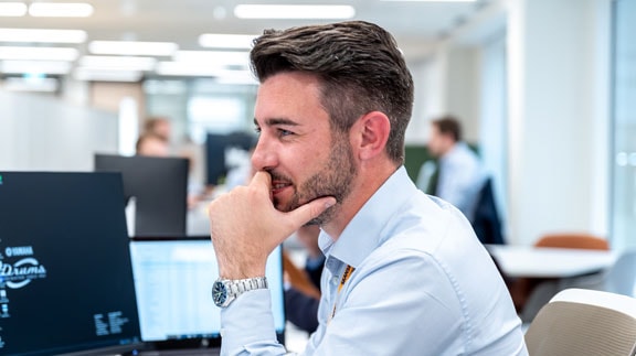 A man in a white shirt works at a computer in a office setting.