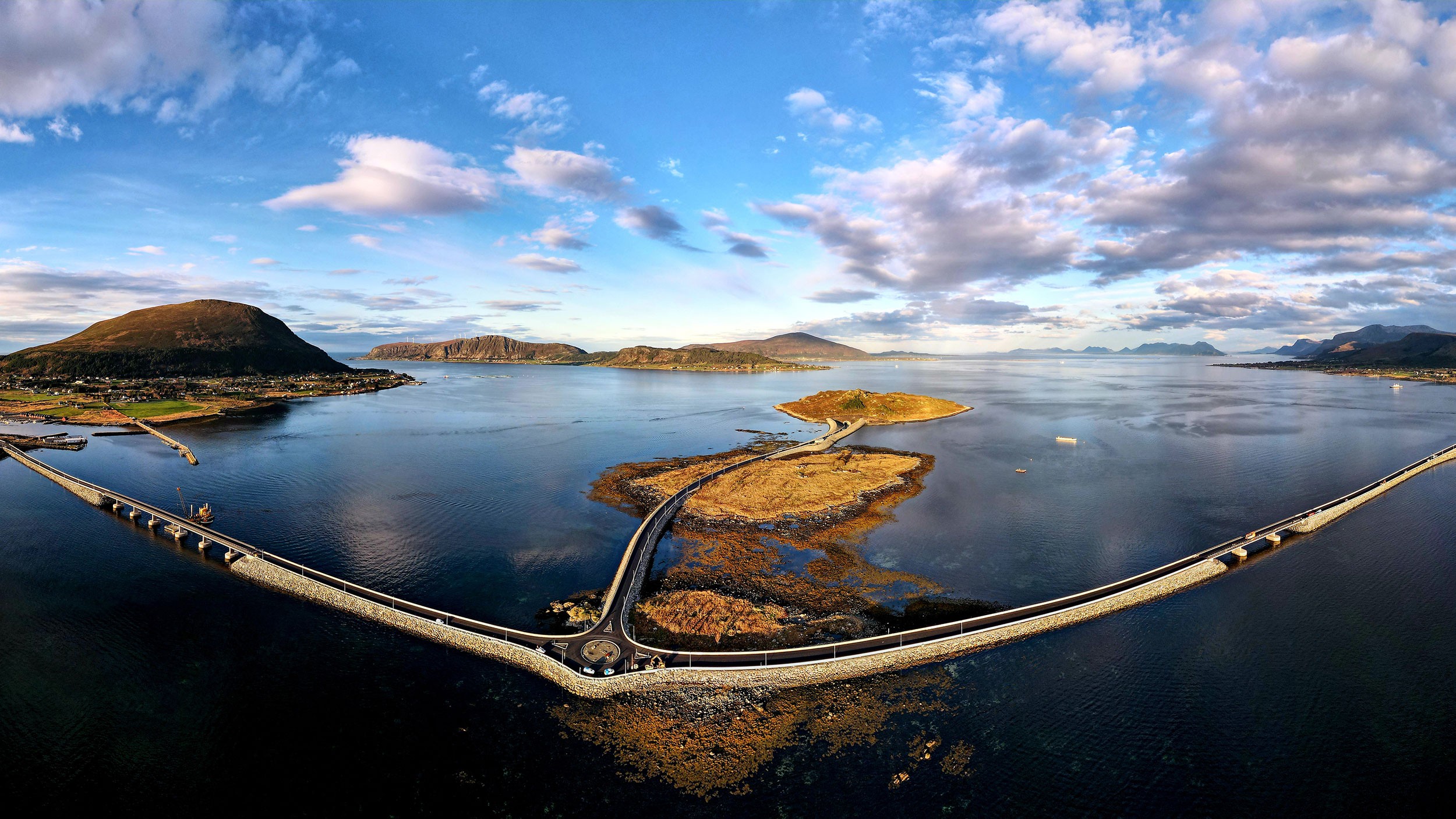 En naturskjønn kystbro langs Nordøyvegen som forbinder øyer under en delvis skyet blå himmel.