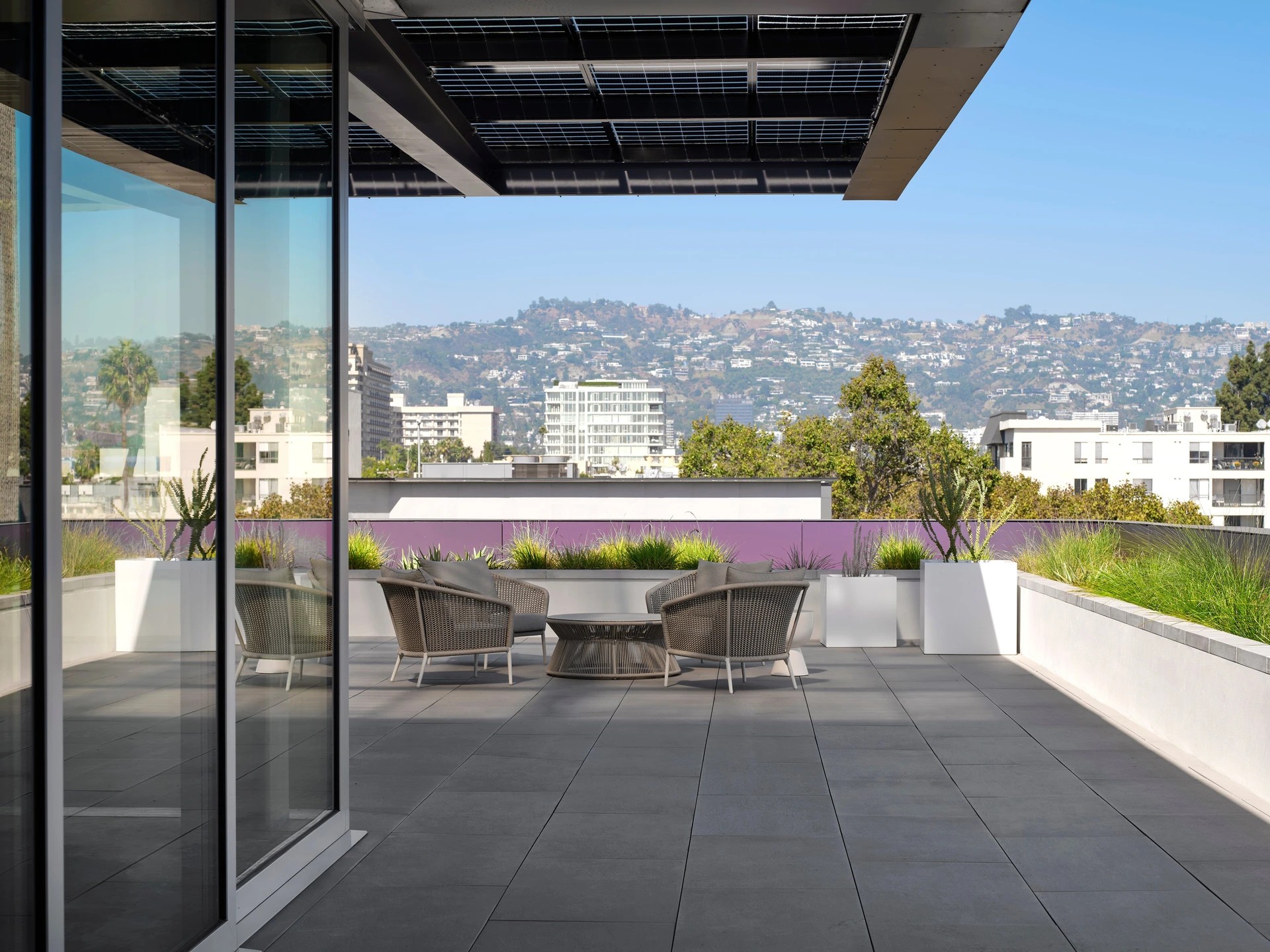Office rooftop patio with city and mountain views on a clear day Office rooftop patio with chairs, table, plants, and city skyline in the background.