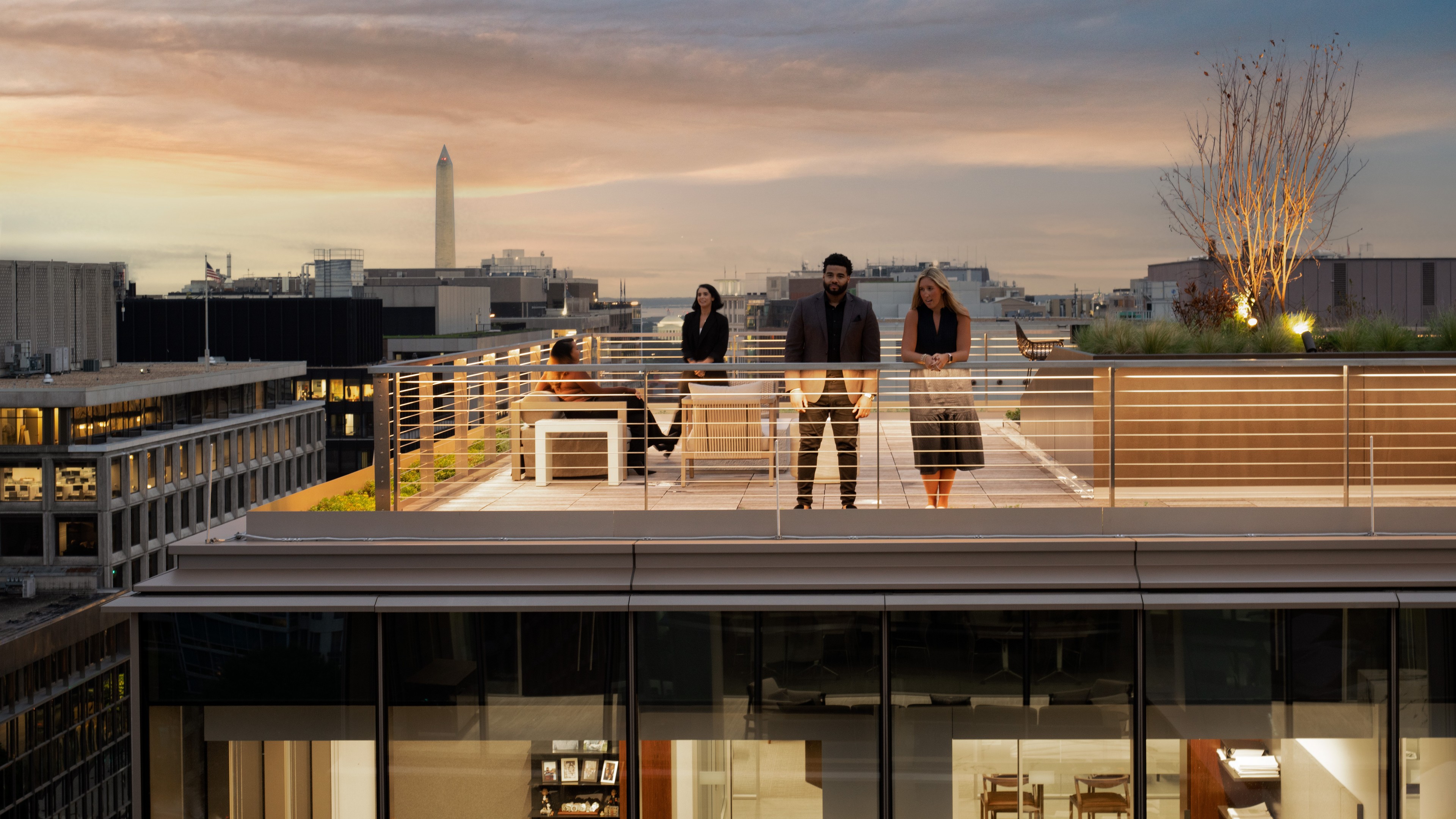 Office Lobby with Stylish Seating and Wooden Accents People socializing on a rooftop terrace with city skyline and Washington Monument.