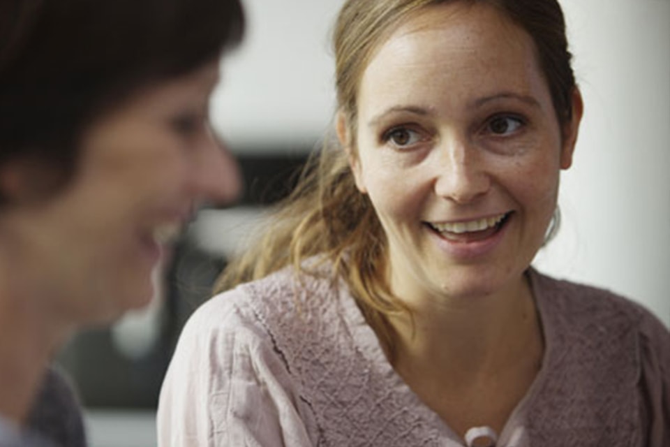 Two colleagues engaged in a serious conversation indoors, wearing casual sweaters.
