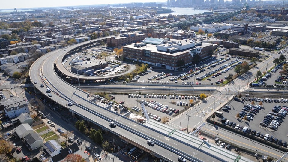 Aerial view of urban highway with surrounding buildings and cars Aerial view of a highway interchange with surrounding parking lots and urban buildings.