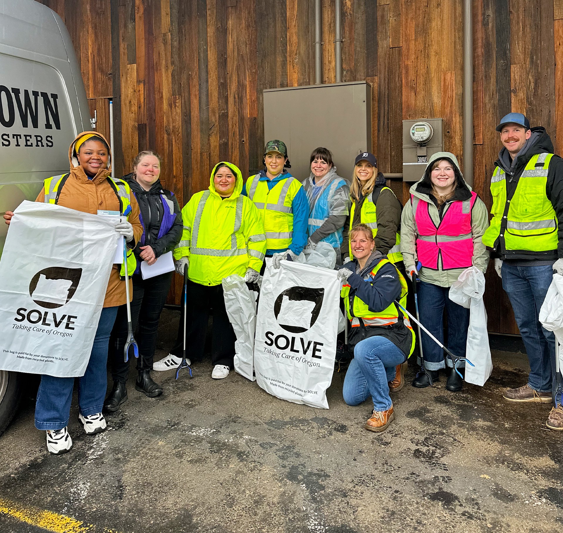 Group of volunteers in safety vests holding trash bags and litter pickers for cleanup.
