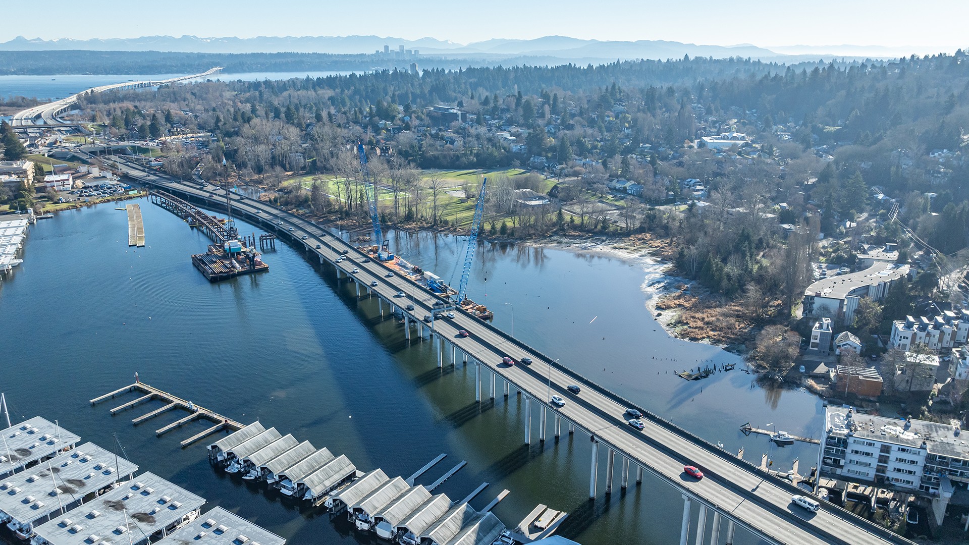 Scenic Aerial View of Bridge and Waterfront in Urban Area Aerial view of a highway bridge over water with boats and forested cityscape in the background.