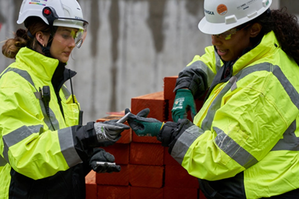 Two construction workers in high-visibility jackets and helmets handling equipment.