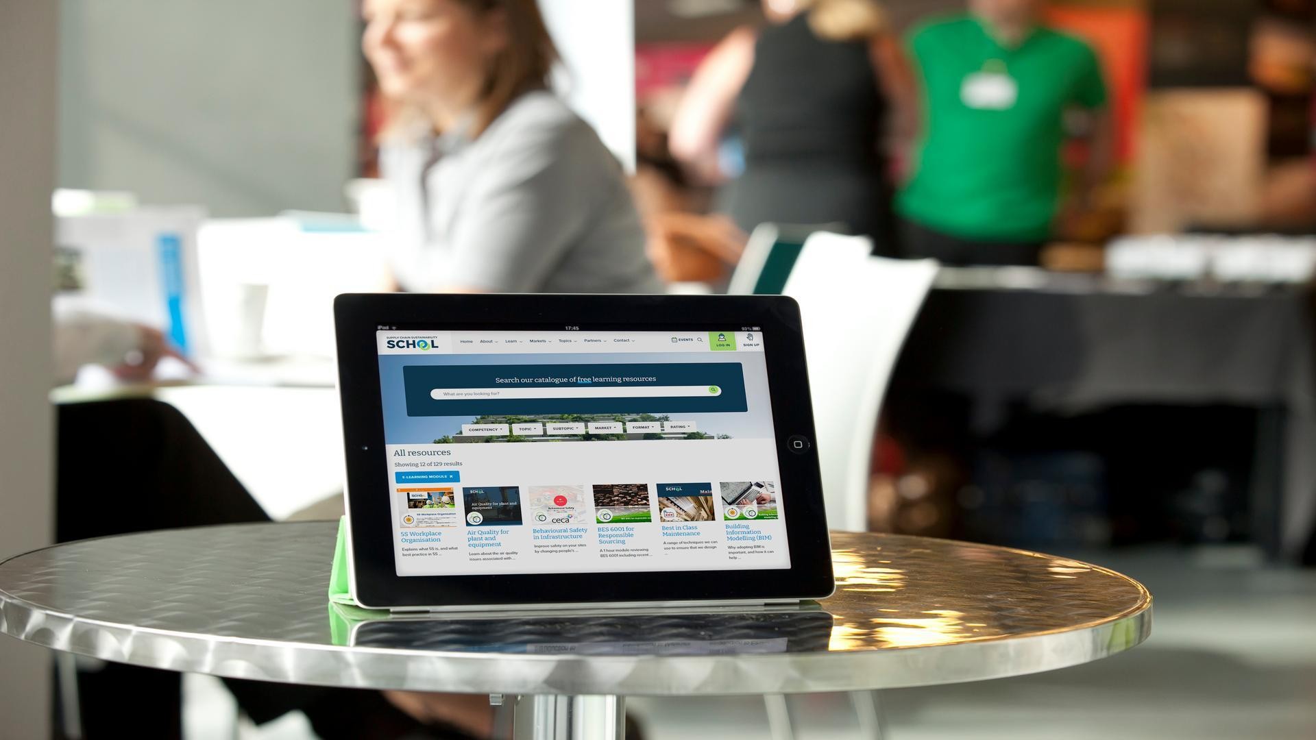 Tablet Displaying Website on Modern Cafe Table Tablet displaying a website on a metallic table in a bright, modern workspace setting.