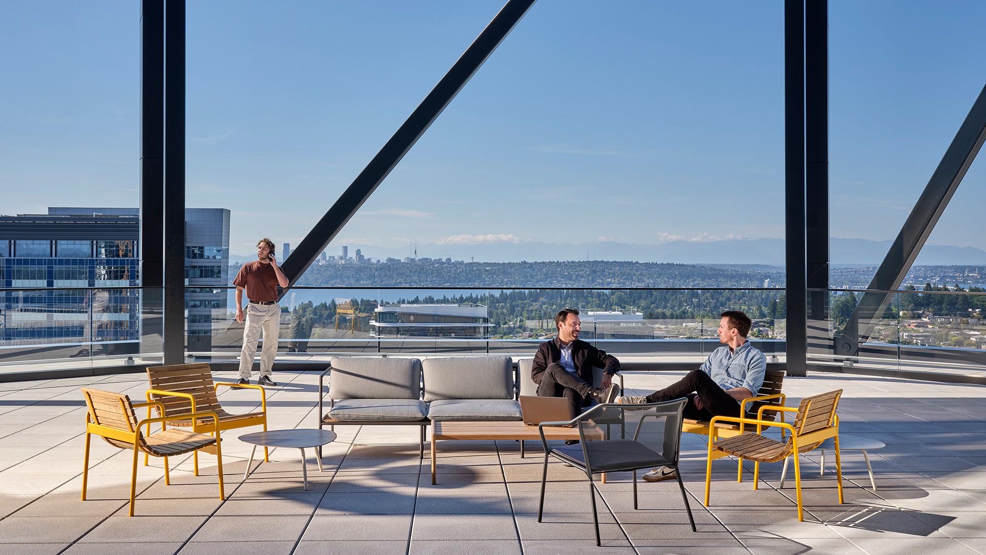 Three men casually talking on a modern rooftop patio with city and water views.