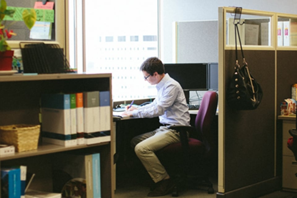 Man working at a desk in an office cubicle with computer and documents.