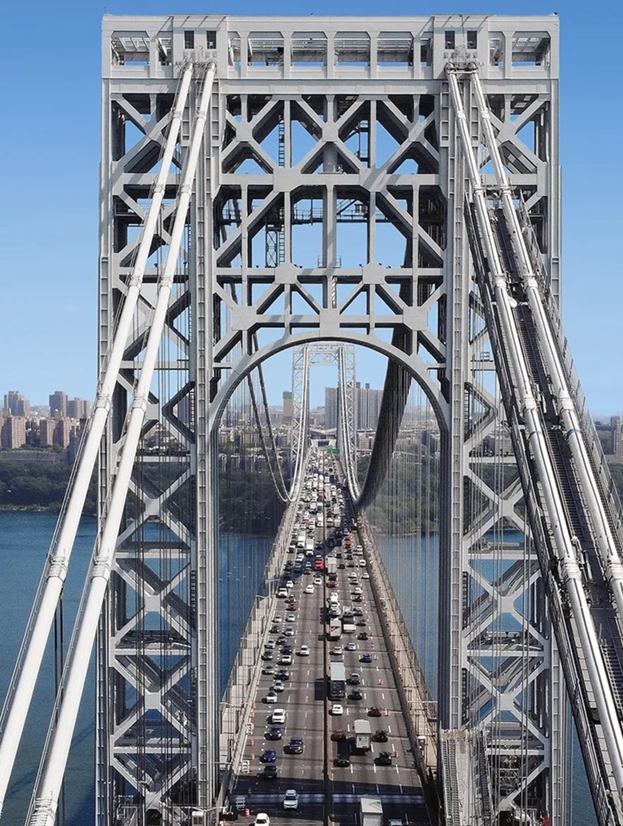 View of a busy suspension bridge with steel towers and traffic over a river in a city.