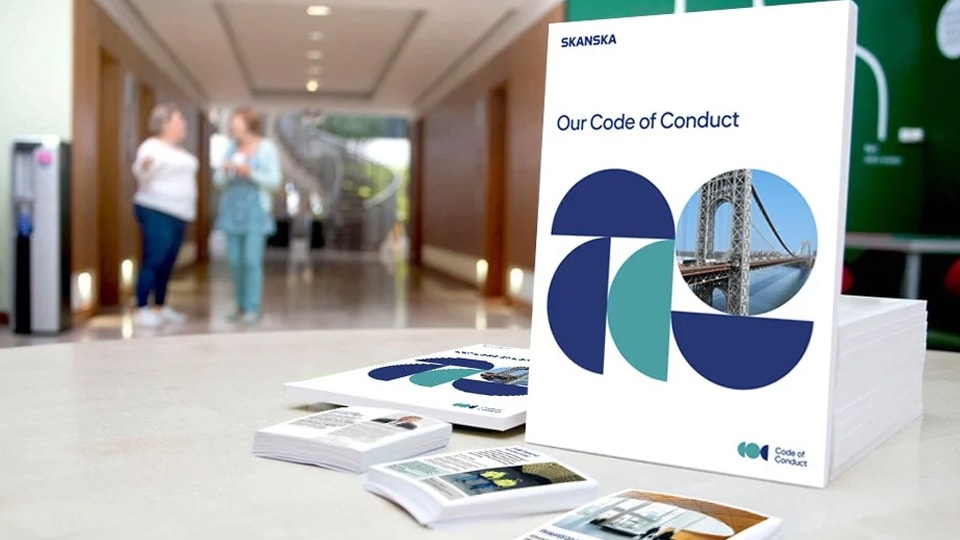 Stack of Skanska's "Our Code of Conduct" booklets displayed on a table in an office hallway.
