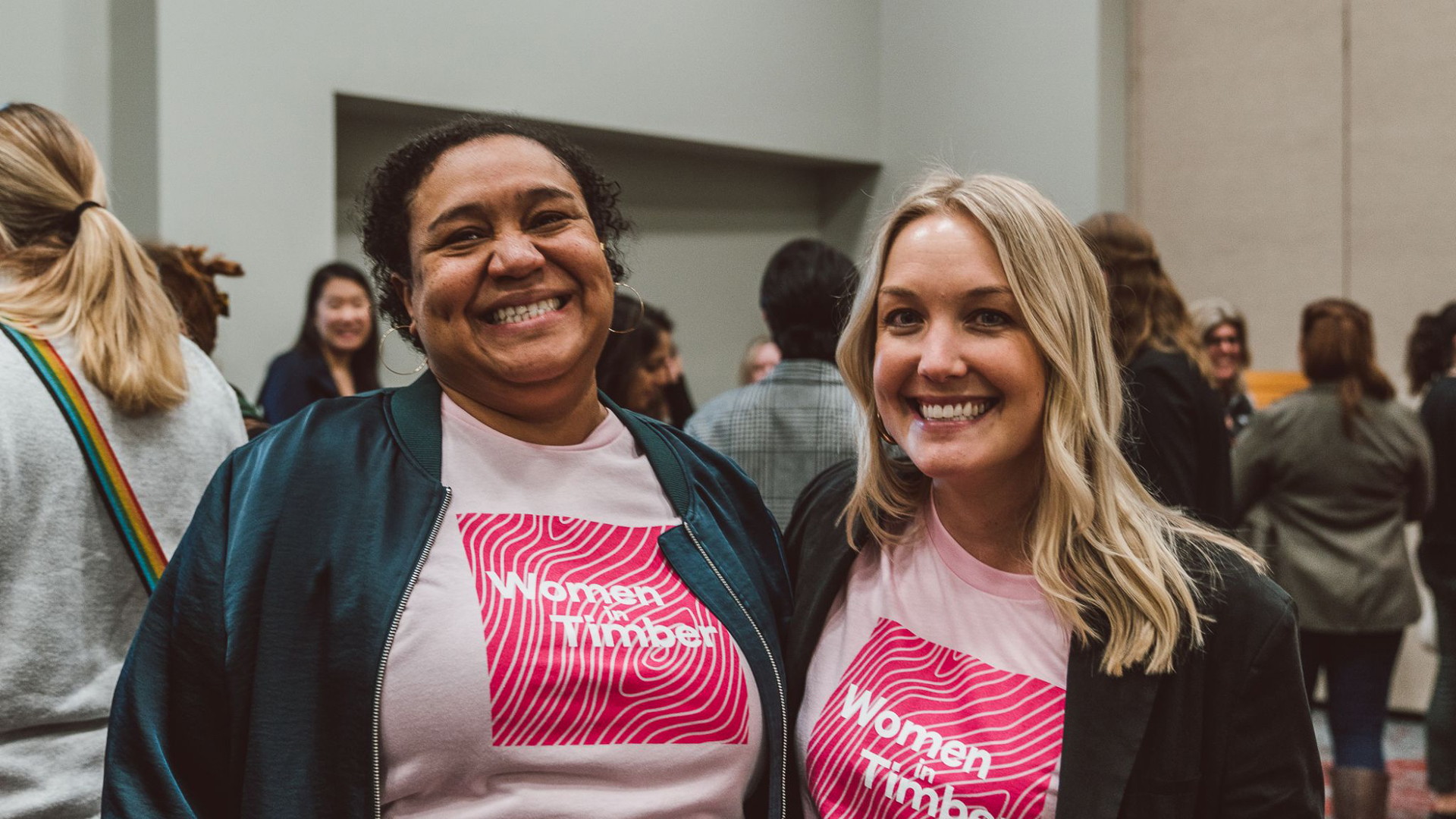 Two women wearing matching pink "Women in Impact" t-shirts at an indoor event.
