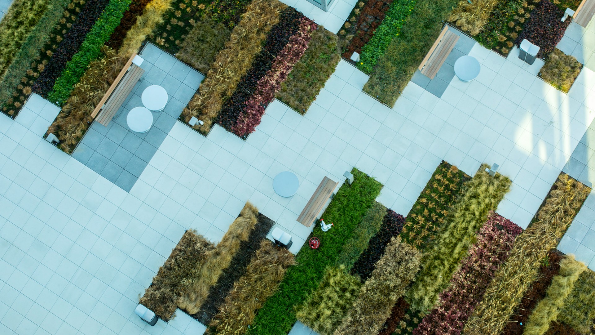 Aerial view of a modern outdoor garden with tiled pathways, benches, and plants.