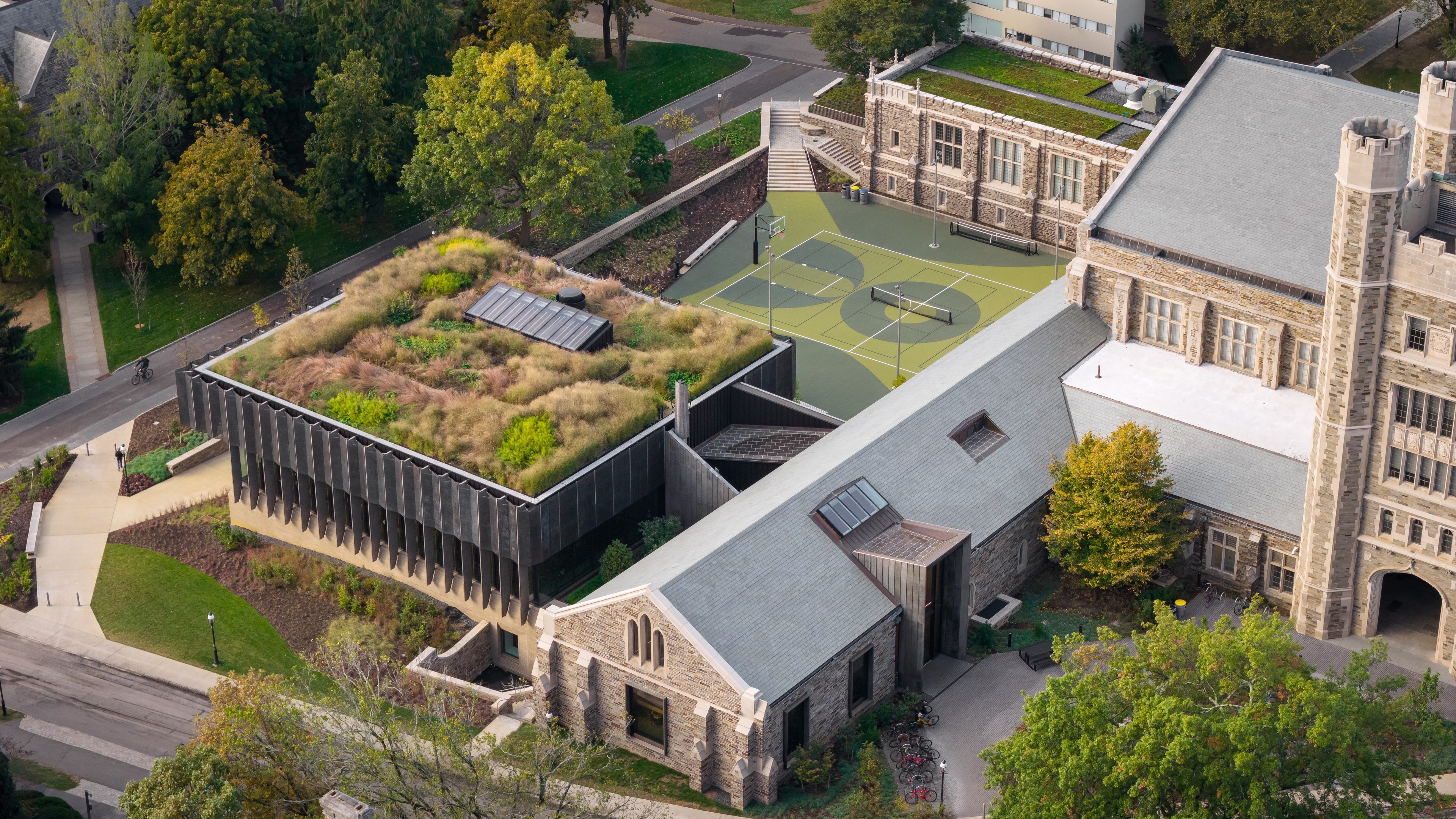Education lab with Orange Chairs and Advanced Equipment Aerial view of a modern building with a green roof and adjacent sports court surrounded by trees.