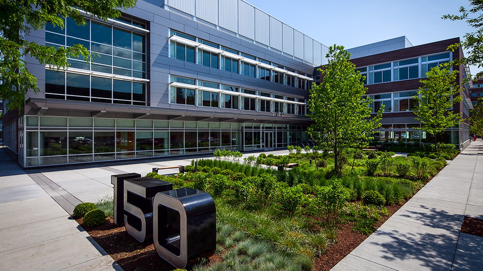 Office Building with Green Courtyard and Clear Skies Office building with large glass windows and landscaped greenery in front.