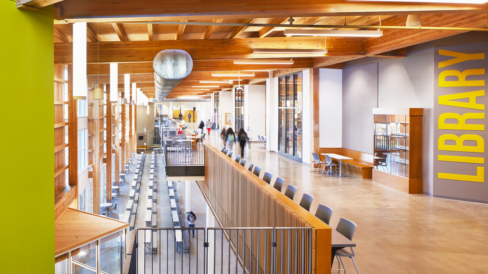 School Library Interior with Wooden Ceiling and Bookshelves Modern library interior with wooden beams, long tables, and seating areas for studying.