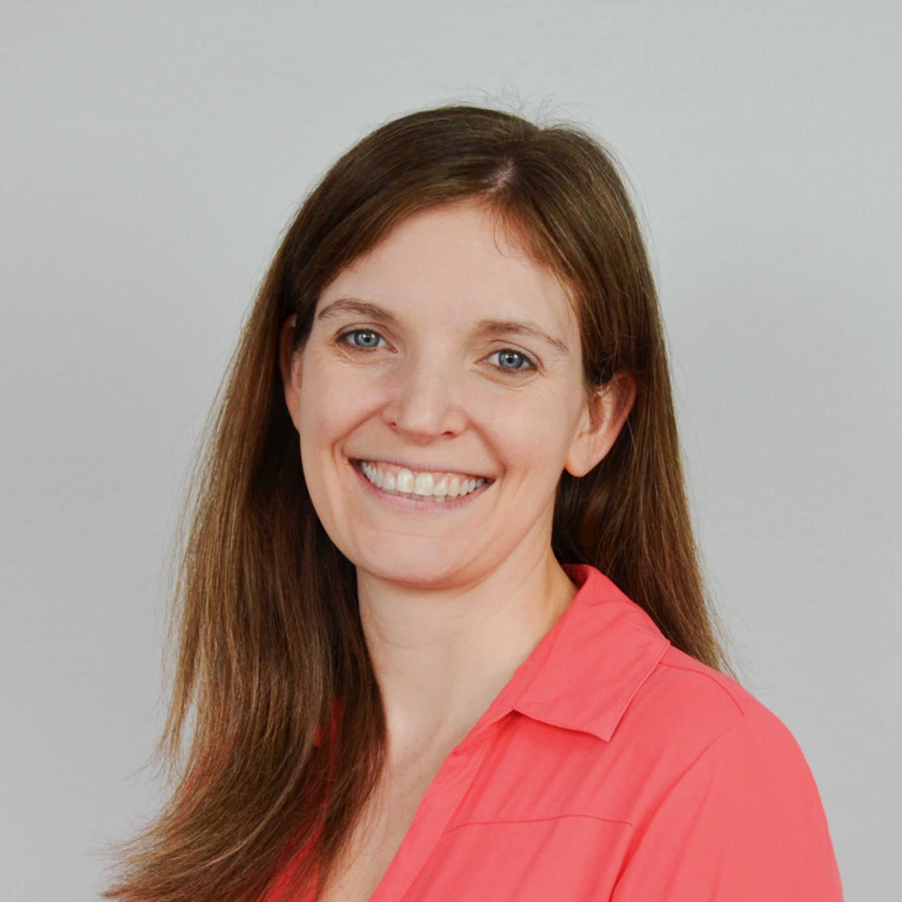 Woman with Long Brown Hair Wearing Coral Shirt on Gray Background Woman with long brown hair wearing a coral blouse against a plain gray background.