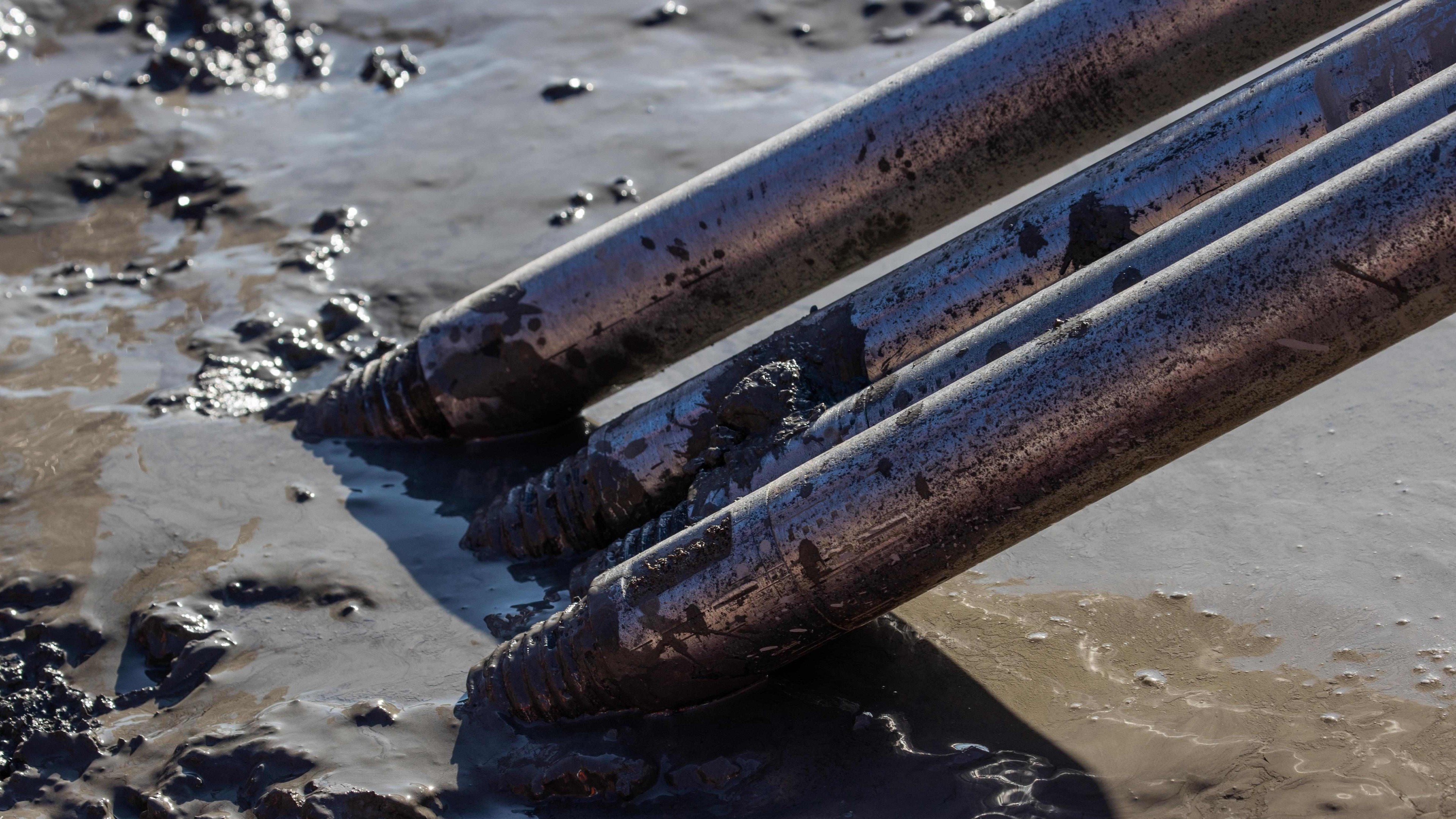 Mud-Covered Drill Bits in Action on Construction Site Close-up of four metal drilling rods partially submerged in muddy water, highlighting their threads.