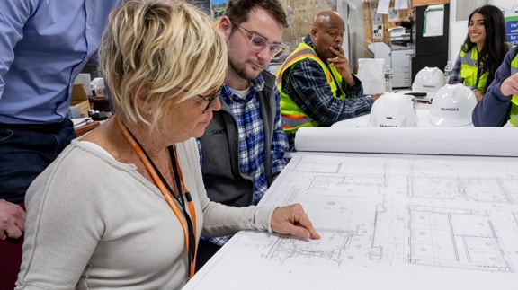 Group of construction professionals reviewing architectural blueprints at a project site.
