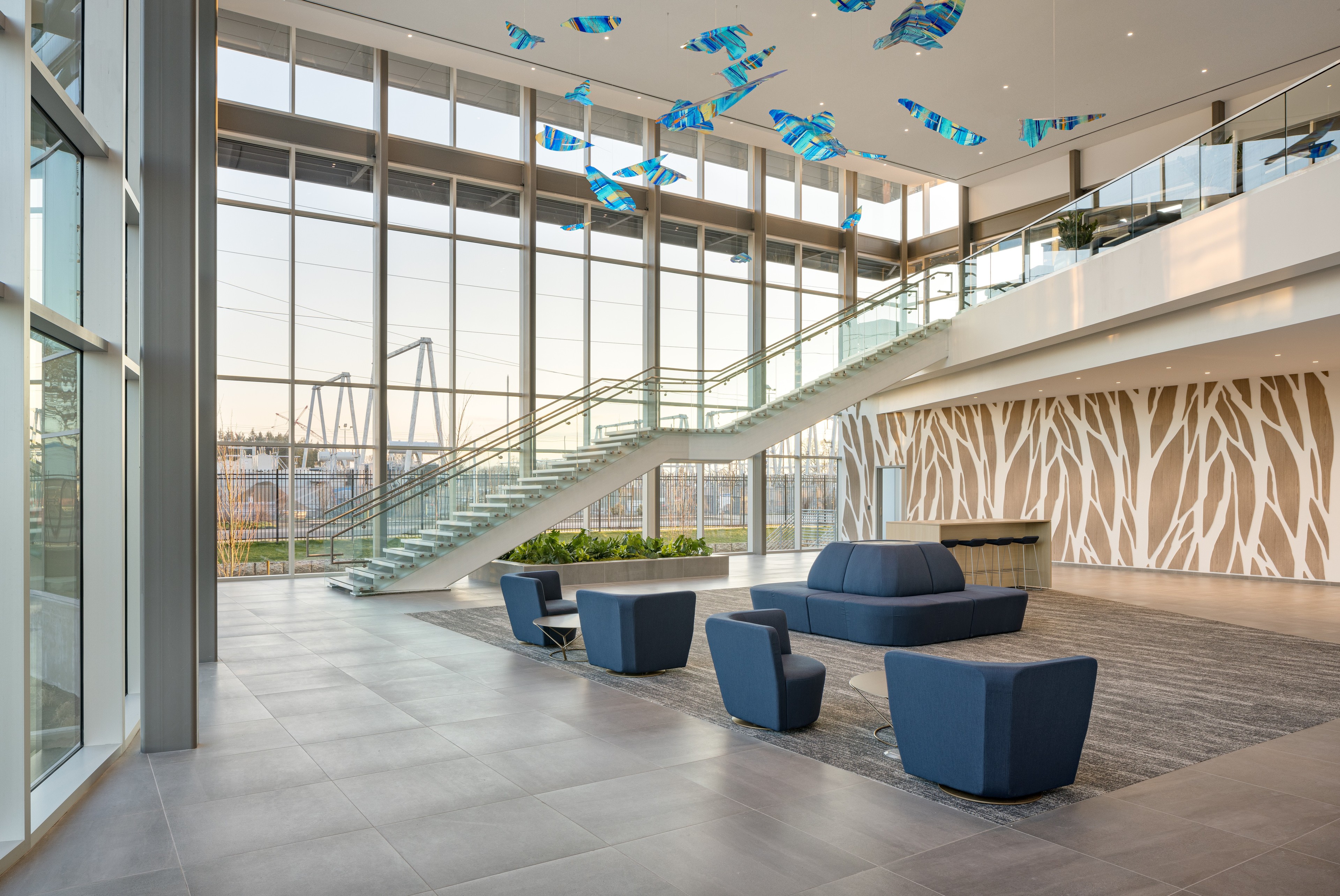 Modern office lobby with large glass windows, blue seating, and artistic ceiling decor.