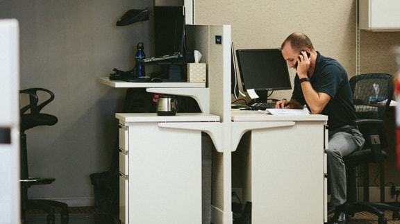 Office workspace with a person on the phone, featuring a computer, desk, and office chair.