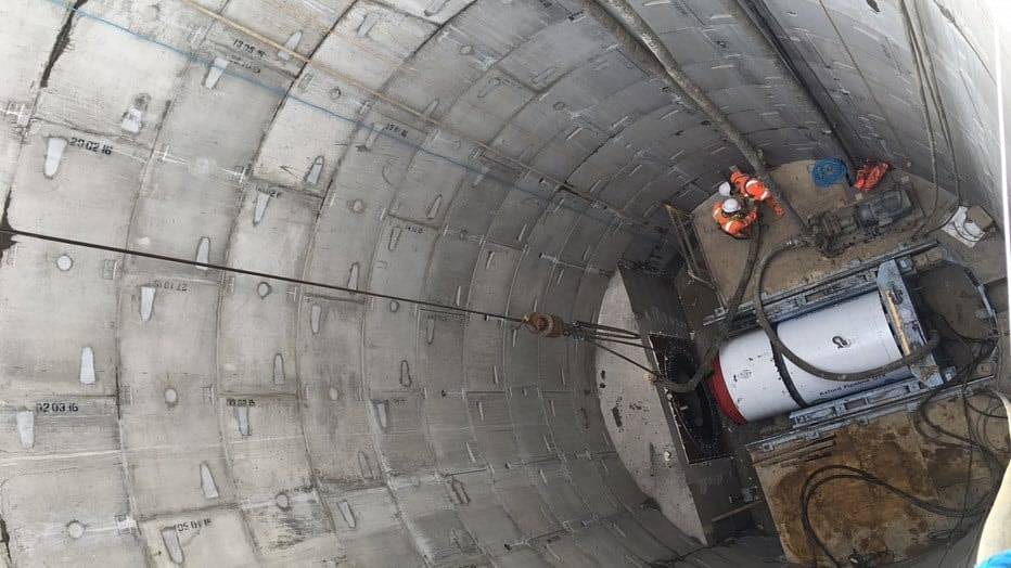 Tunnel Construction with Workers and Machinery Inside Construction workers inside a large cylindrical tunnel with machinery and concrete walls.