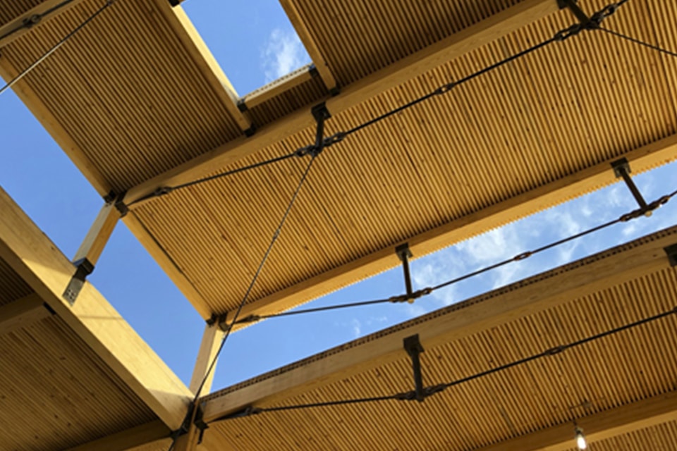 Wooden roof structure with metal support beams and clear blue sky visible through gaps.
