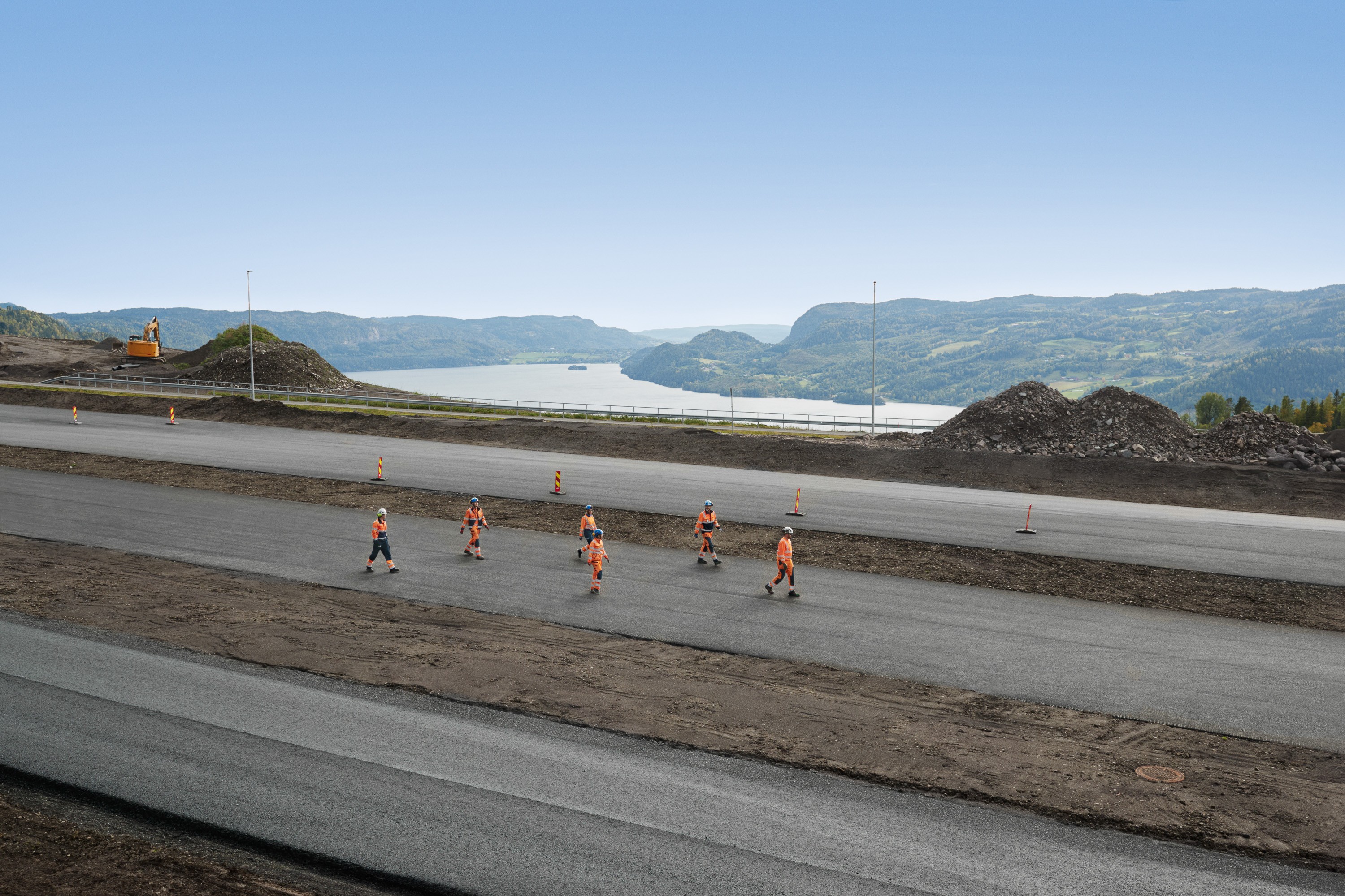 Construction workers paving a road with scenic mountain view To bygningsarbeidere i oransje sikkerhetsutstyr hviler ved en betongtunnelinngang på en asfaltert vei.
