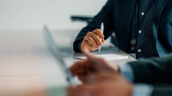 Business meeting scene with a person holding a pen and taking notes at a desk.