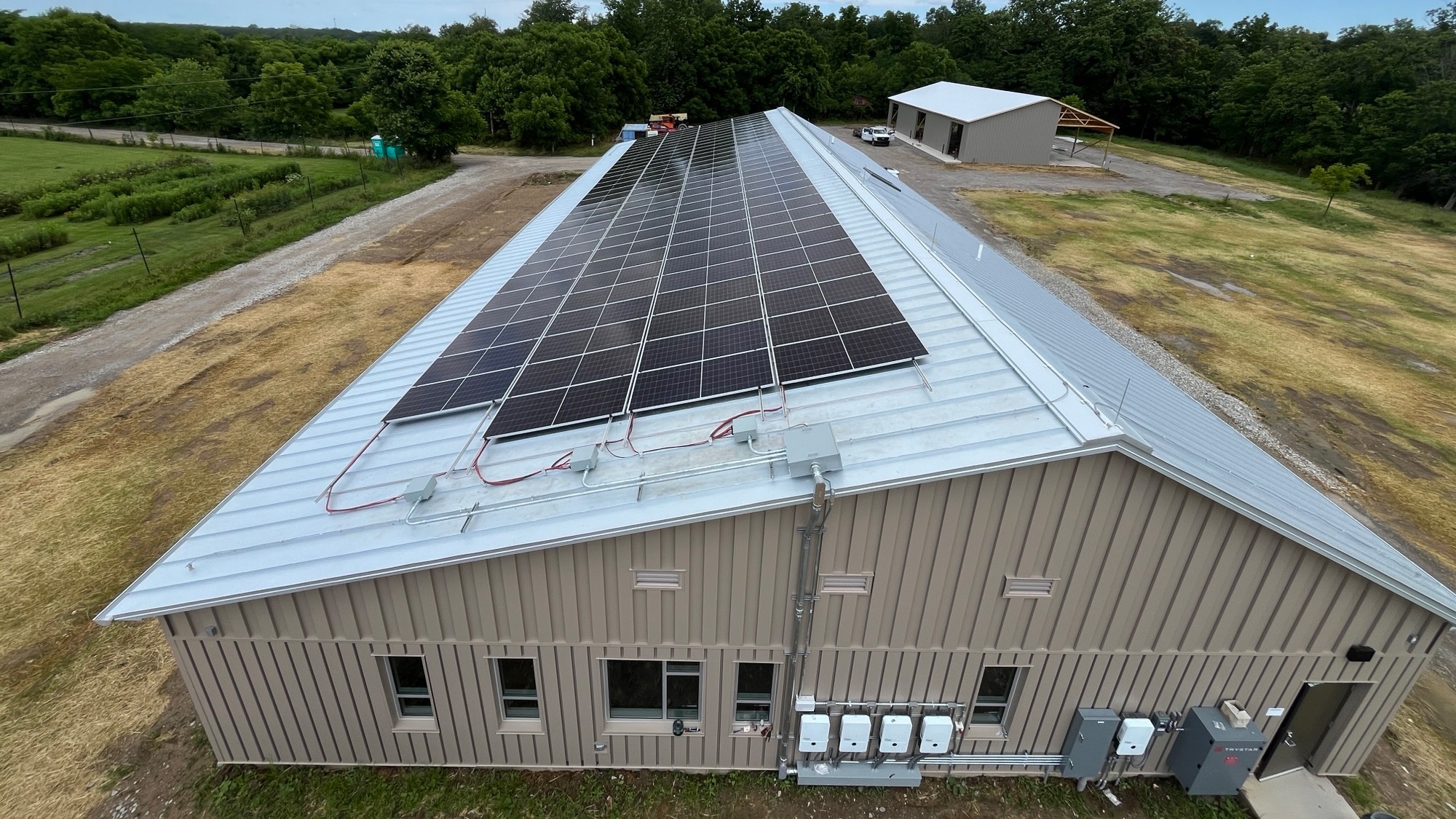 Solar Panels Installed on Metal Roof of Industrial Building Solar panels installed on the metal roof of a large industrial building surrounded by trees.