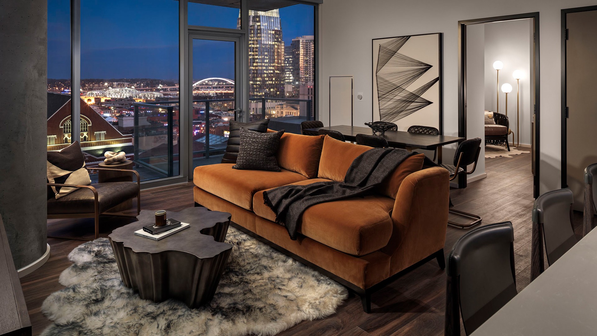 Residential Lobby with Elegant Design and Natural Lighting Modern living room with a brown sofa, abstract art, and city skyline view at night.