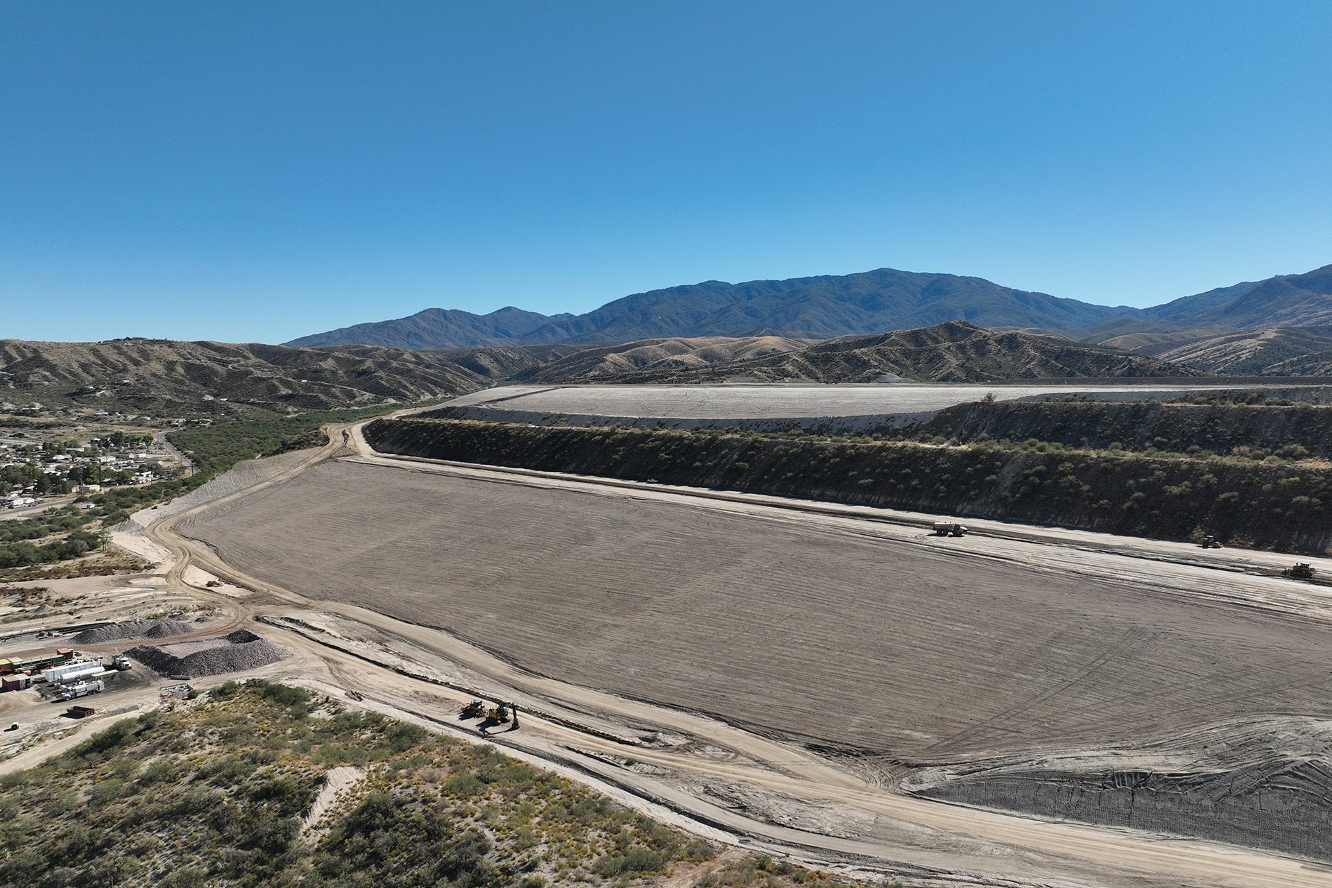 Large Construction Site with Mountain Background under Clear Sky Large construction site with earthmoving equipment and mountainous landscape under clear sky.